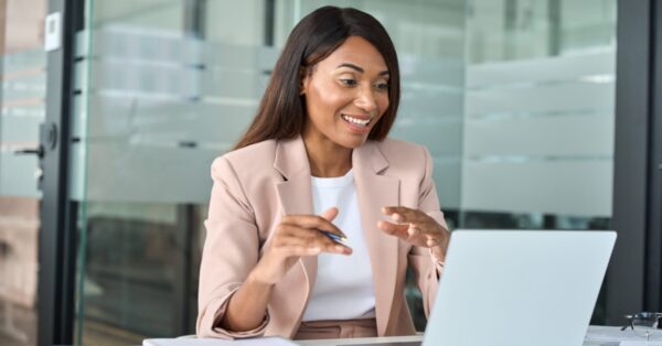 Young professional woman sitting at desk taking video call on laptop