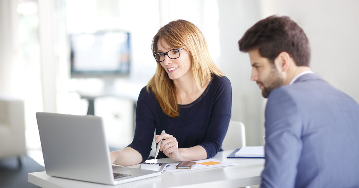 Two people sitting at a desk looking at a laptop