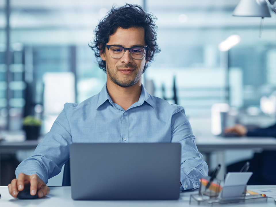 Modern Office Businessman Working on Computer. Portrait of Successful Latin IT Software Engineer Working on a Laptop at his Desk. Diverse Workplace with Professionals. Front View Shot